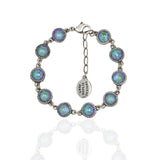 The Simple Drops Pacific Opal Bracelet by Anne Koplik Designs, Inc. features round iridescent stones in decorative bezels, link connections, an adjustable chain, and a small oval tag with engraved text.