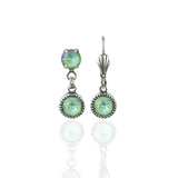 The Simple Drop Silky Sage Delite Earrings by Anne Koplik Designs, Inc. are USA-made silver earrings with round, iridescent green stones—one earring features a single stone, the other two stones set vertically in decorative bezels.
