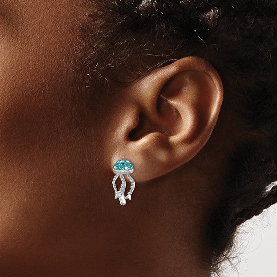 A close-up of a person’s ear wearing Presco/Quality Gold’s Crystal Jellyfish Post Earrings—sterling silver jewelry featuring jellyfish with blue gemstone bodies and silver tentacles. The person’s curly hair is pulled back.