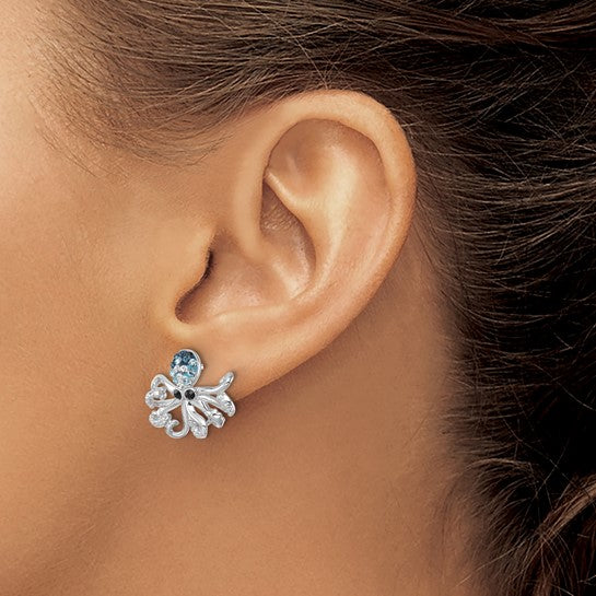 A close-up of a womans ear wearing Presco/Quality Gold Crystals Octopus Earrings, featuring detailed sterling silver tentacles and a sparkling blue crystal head.