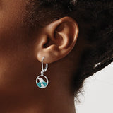 A close-up of a person with dark skin and braided hair wearing the Presco/Quality Gold Crystal Wave Whitecap Earrings—sterling silver hoops with circular pendants featuring blue and white gemstone accents.