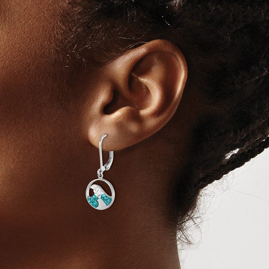 A close-up of a person with dark skin and braided hair wearing the Presco/Quality Gold Crystal Wave Whitecap Earrings—sterling silver hoops with circular pendants featuring blue and white gemstone accents.