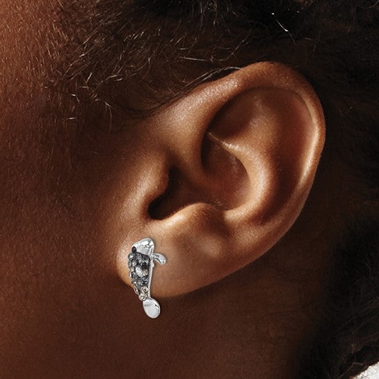 Close-up of a medium-brown ear wearing Presco/Quality Golds Crystal Manatee Post Earrings—sterling silver studs shaped like manatees, featuring small dark gemstones and metallic accents. Hair is visible at the top.