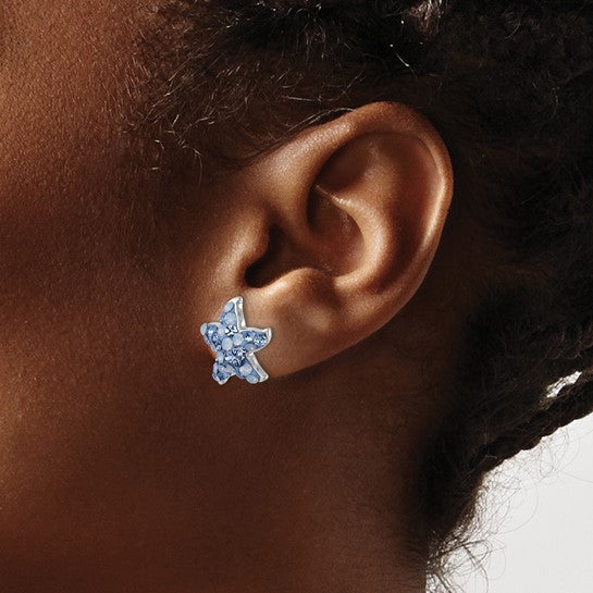Close-up of a persons ear wearing Presco/Quality Gold Crystal Blue & Clear Starfish Post Earrings—silver star-shaped studs with blue and clear accents, set against a neutral background.