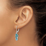 A close-up of a woman with light to medium skin and pulled-back hair wearing Presco/Quality Golds Crystal Flip Flop Dangle Earrings, sterling silver earrings adorned with blue crystals and shaped like flip-flop sandals.