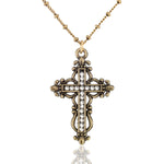 The Anne Koplik Designs Brass Filigree Crystal Cross Necklace features an ornate, vintage-style crystal-lined cross pendant, displayed on a reflective white background.