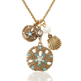 The Sand Dollar, Shell & Pearl Beach Charm Jumble Necklace by Anne Koplik Designs, Inc. features a large sand dollar pendant with seashell, pearl, and gem charms accented by blue and white stones for a breezy seaside look.