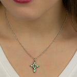 Someone wears the Anne Koplik Designs, Inc. Small Stone Fancy Cross Pacific Opal Necklace, featuring a delicate beaded silver chain and a cross-shaped pendant with crystal accents, shown against fair skin and a white top.