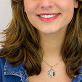 A smiling woman with wavy brown hair wears a denim jacket and the Crescent Moon w/Black Cat Necklace by Anne Koplik Designs, Inc., standing against a plain light background.