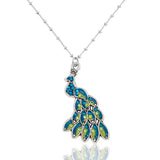 The Whimsy Stone & Enamel Male Peacock Necklace by Anne Koplik Designs features a peacock pendant adorned with blue and green gemstones, hand-enameled details, and hangs from a delicate beaded chain.