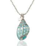 The Anne Koplik Designs, Inc. Turquoise Enamel Pearl Seashell Jumble Necklace features a silver chain with a blue and white seashell pendant and a small pearl, capturing ocean-inspired beauty on a white display.