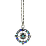The Whimsy Fancy Blue Compass Necklace by Anne Koplik Designs, Inc. features a silver compass pendant with blue and turquoise gemstones, cardinal direction letters, a starburst center, and hangs from a silver chain.