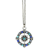 The Whimsy Fancy Blue Compass Necklace by Anne Koplik Designs, Inc. features a silver compass pendant with blue and turquoise gemstones, cardinal direction letters, a starburst center, and hangs from a silver chain.