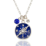 The Anne Koplik Designs, Inc. NK: Blue Enamel & Stone Compass Jumble is a silver necklace featuring a blue enamel compass pendant marked N, S, E, W, with a blue bead and clear gemstone charm on a delicate chain.