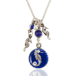 The Blue Enamel Disc w/Seahorse Necklace by Anne Koplik Designs, Inc. features silver seahorse charms, a round blue gemstone, and a larger blue enamel pendant with a silver seahorse and crystal—a stylish beach-inspired piece.