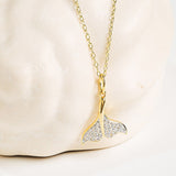 The Shanore Gold Vermeil & White Sapphire Whale Tail Mini Necklace is displayed against a white, textured background.