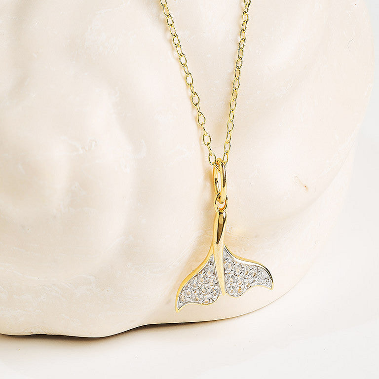 The Shanore Gold Vermeil & White Sapphire Whale Tail Mini Necklace is displayed against a white, textured background.