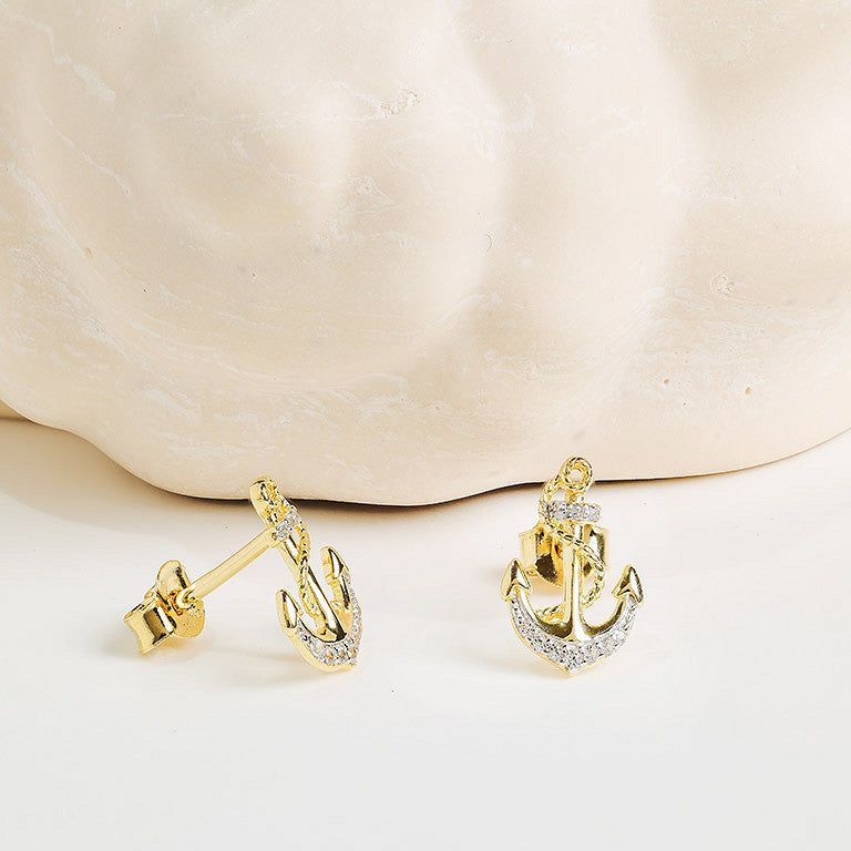 Shanore's Gold Vermeil & White Sapphire Anchor Post Earrings, displayed on light beige marble, feature sparkling white sapphires—a stunning nautical jewelry piece.