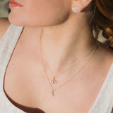 A woman in a cream sleeveless top wears the Shanore Gold Vermeil & White Sapphire Sun Mini Necklace layered with another necklace and small round stud earrings for a delicate, sparkling look.