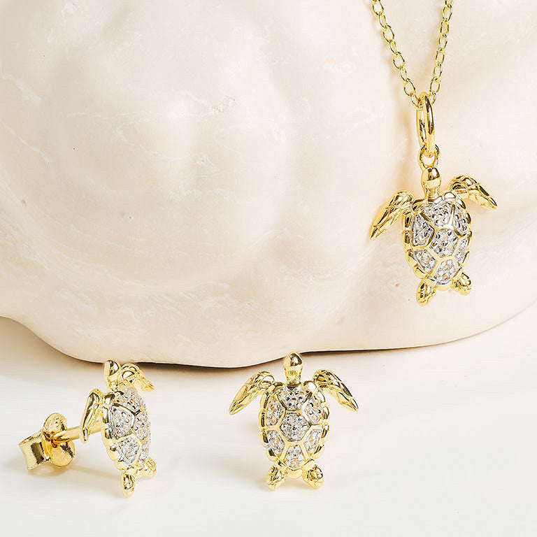 The Shanore Gold Vermeil & White Sapphire Turtle Mini Necklace features a sparkling turtle pendant on a chain, crafted in 925 sterling silver, shown against a light textured background.