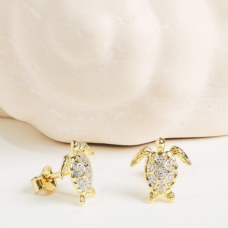 Shanore Gold Vermeil & White Sapphire Turtle Post Earrings are shown against a smooth, cream-colored shell background.