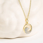 The Shanore Gold Vermeil & White Sapphire Wave Mini Necklace features a round pendant half encrusted with sparkling white sapphires, displayed on a light cream stone background.