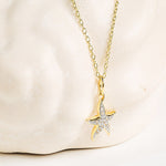 The Shanore Gold Vermeil & White Sapphire Starfish Mini Necklace features a shimmering starfish pendant, shown against a marble-inspired background.