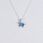 The Mosaico/.925 NK: Mosaic Mini Waving Turtle Aurora A pendant features a silver turtle with a blue and green gemstone shell, shown on a light gray background.