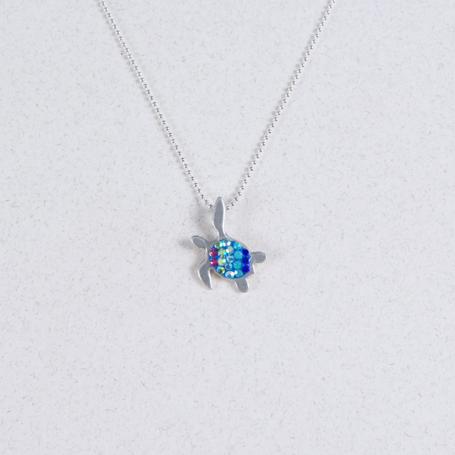 The Mosaico/.925 NK: Mosaic Mini Waving Turtle Aurora A pendant features a silver turtle with a blue and green gemstone shell, shown on a light gray background.