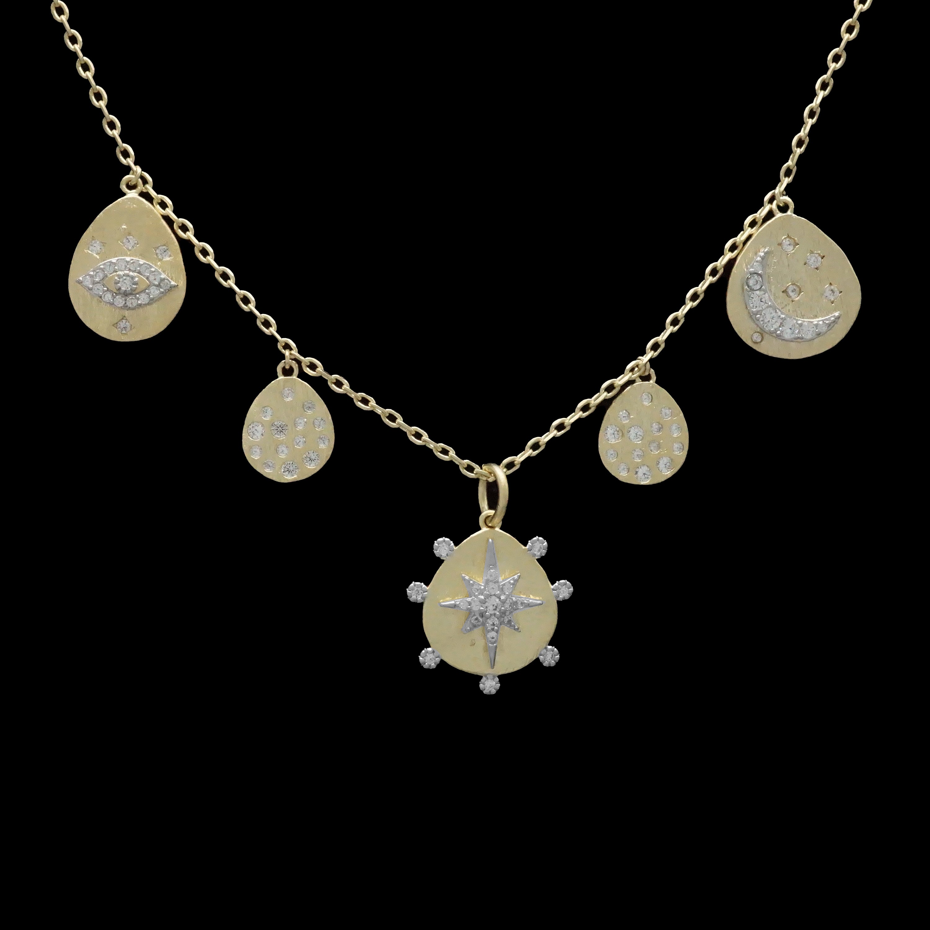 The Be-Je Designs Gold Charms Evil Eye Necklace features five 14kt gold charms—an eye, crescent moon with stars, sunburst, and two teardrops—set against black with sparkling cubic zirconia for a bold look.