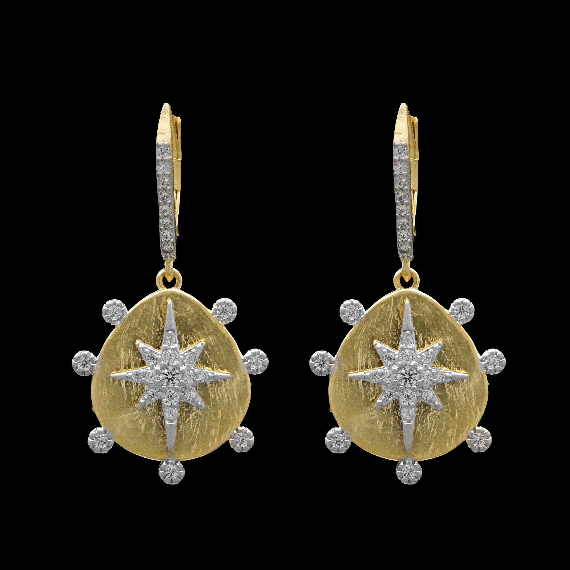 Be-Je Designs’ Matte Gold Disc CZ Star Earrings feature a textured matte gold disc with a central starburst and sparkling cubic zirconia accents, beautifully contrasted against a black background.