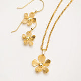 The Plumeria Drop Gold Necklace by Holly Yashi features hand-formed five-petal blooms with a textured finish, delicate chain, and gold bead centers, displayed with matching earrings from Holly Yashi Jewelry.