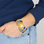 A person in light blue jeans and a navy sweater has their hand in their pocket, highlighting the Holly Yashi Selena Midnight Blue Bracelet—an elegant gold piece with sunburst motifs that brings celestial charm to their wrist.