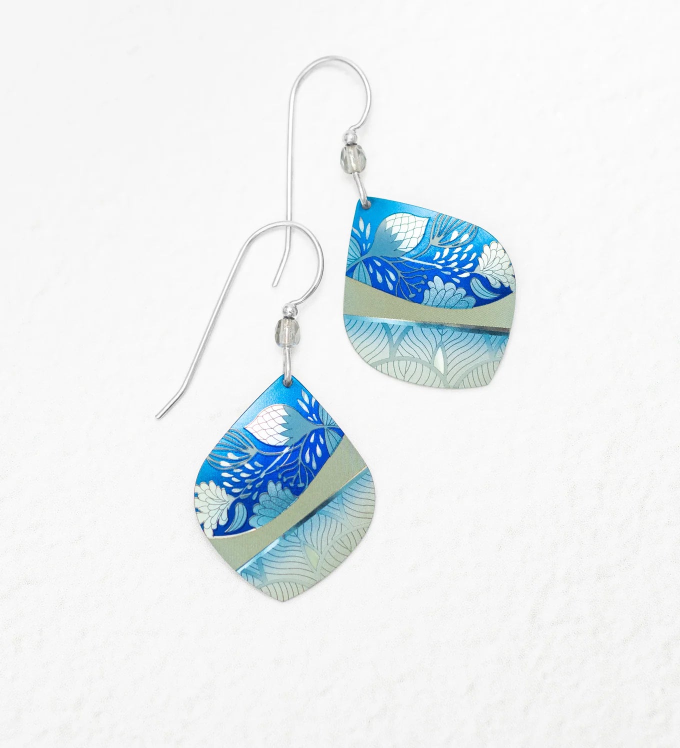 The Lani Kai Blue Earrings by Holly Yashi feature handcrafted square dangles with silver hooks, displaying blue, light blue, and gray floral and leaf patterns on a white textured background.