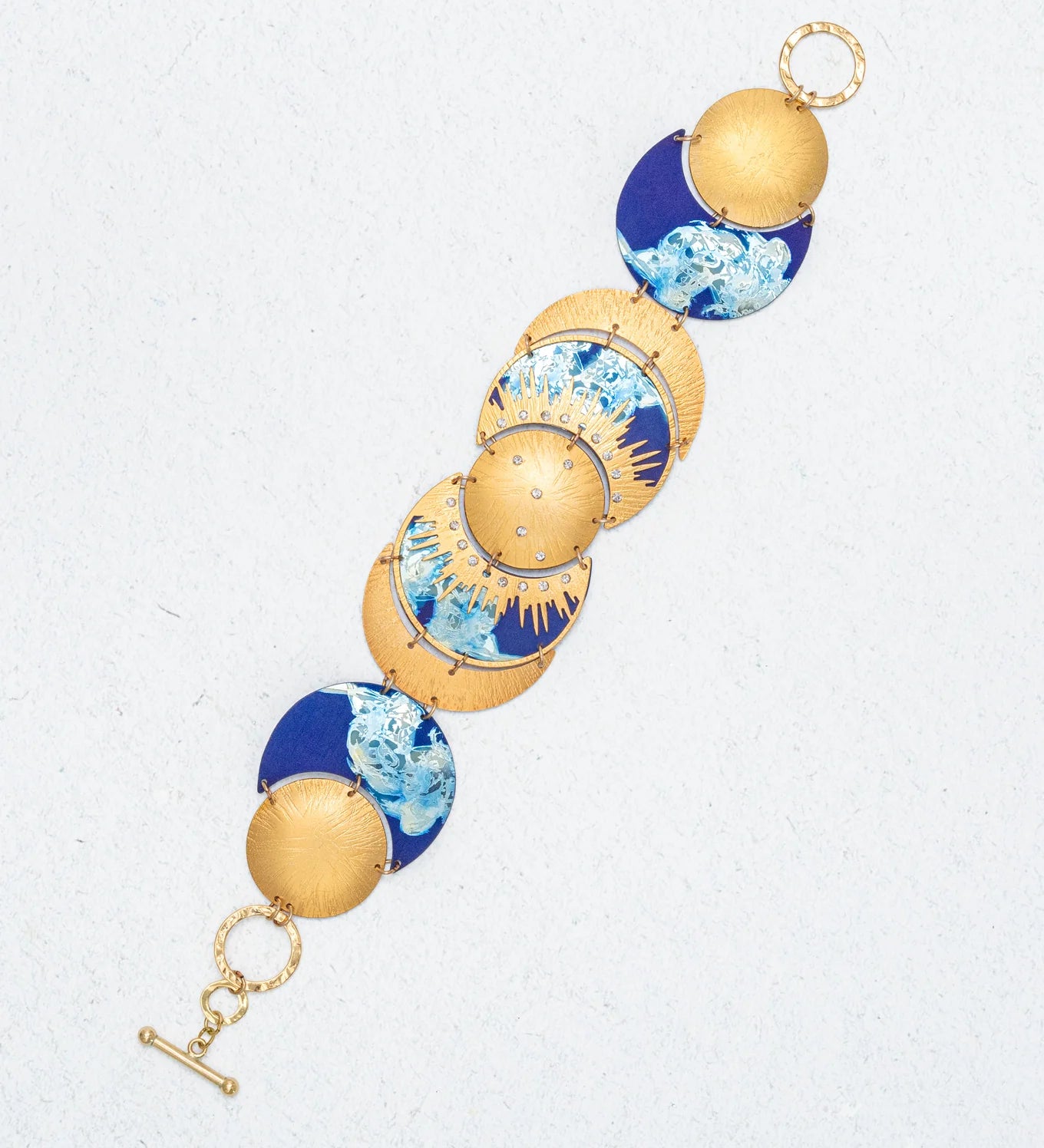 The Selena Midnight Blue Bracelet by Holly Yashi showcases round, domed segments with blue and white marbled designs and a toggle clasp, all displayed on a light textured background for celestial charm.