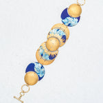 The Selena Midnight Blue Bracelet by Holly Yashi showcases round, domed segments with blue and white marbled designs and a toggle clasp, all displayed on a light textured background for celestial charm.