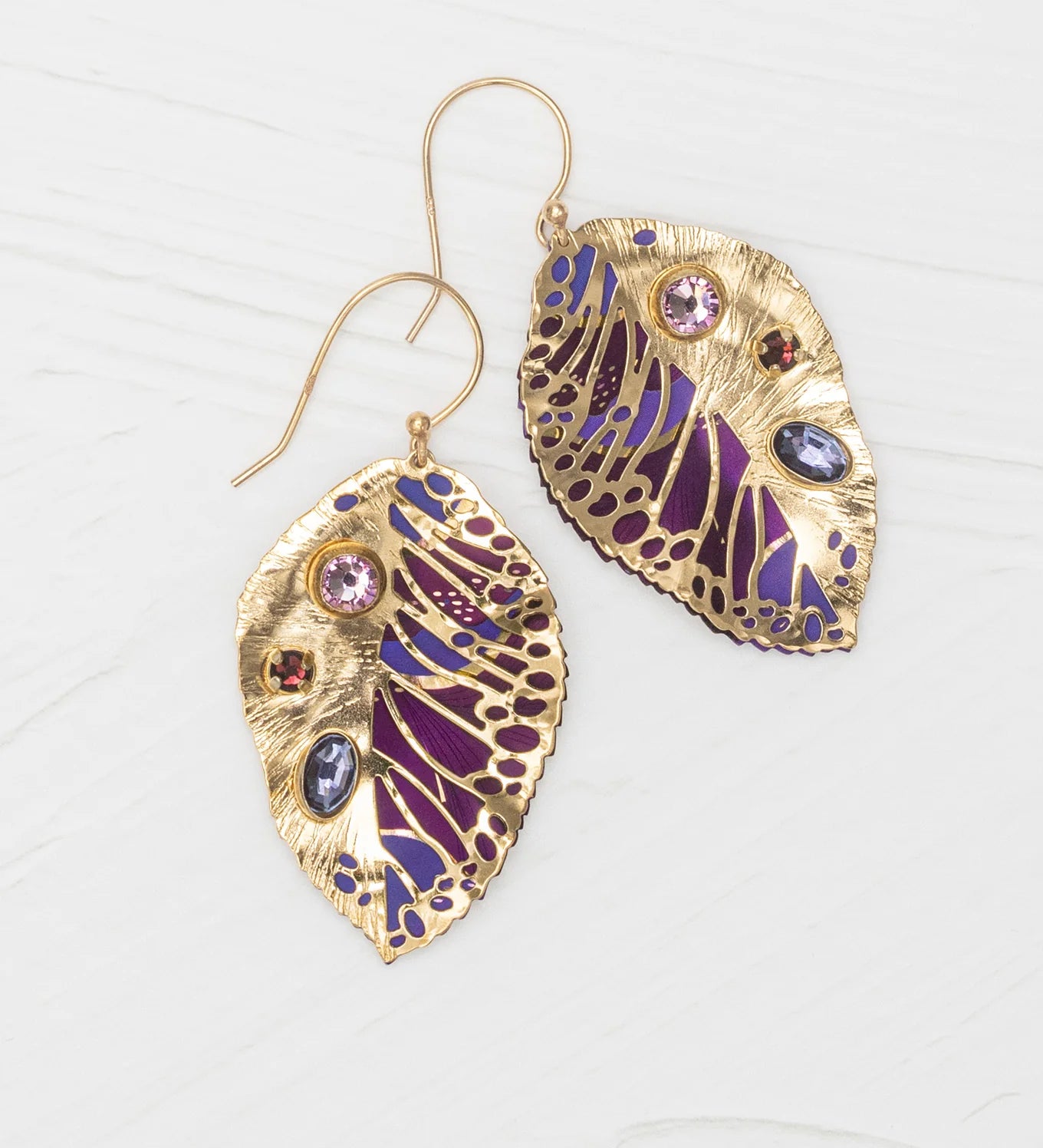 Perennial Elm Purple Earrings by Holly Yashi, gold leaf-shaped with detailed purple and blue enamel and colorful gemstones, displayed on a light wooden surface.