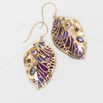 Perennial Elm Purple Earrings by Holly Yashi, gold leaf-shaped with detailed purple and blue enamel and colorful gemstones, displayed on a light wooden surface.