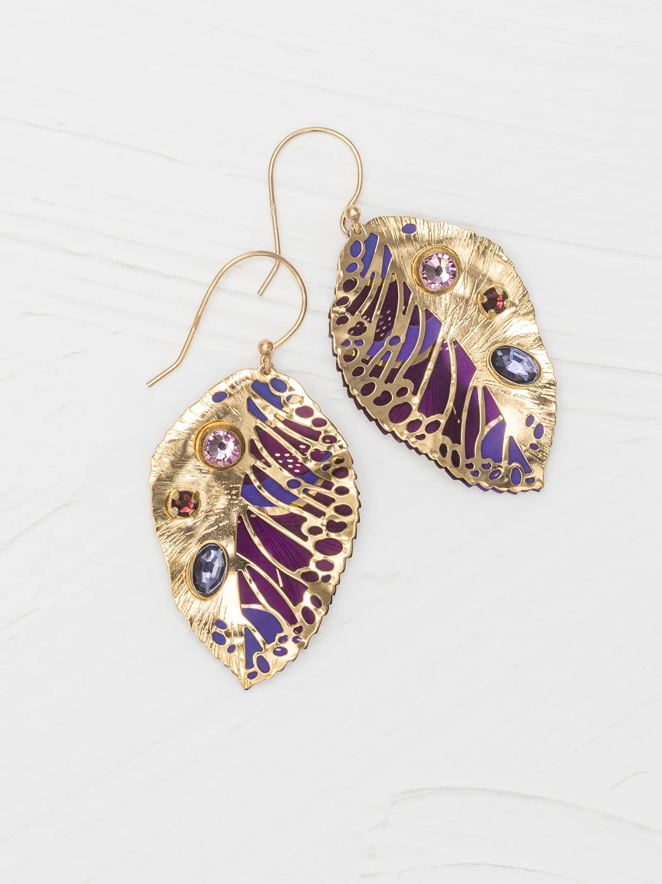 Perennial Elm Purple Earrings by Holly Yashi, gold leaf-shaped with detailed purple and blue enamel and colorful gemstones, displayed on a light wooden surface.