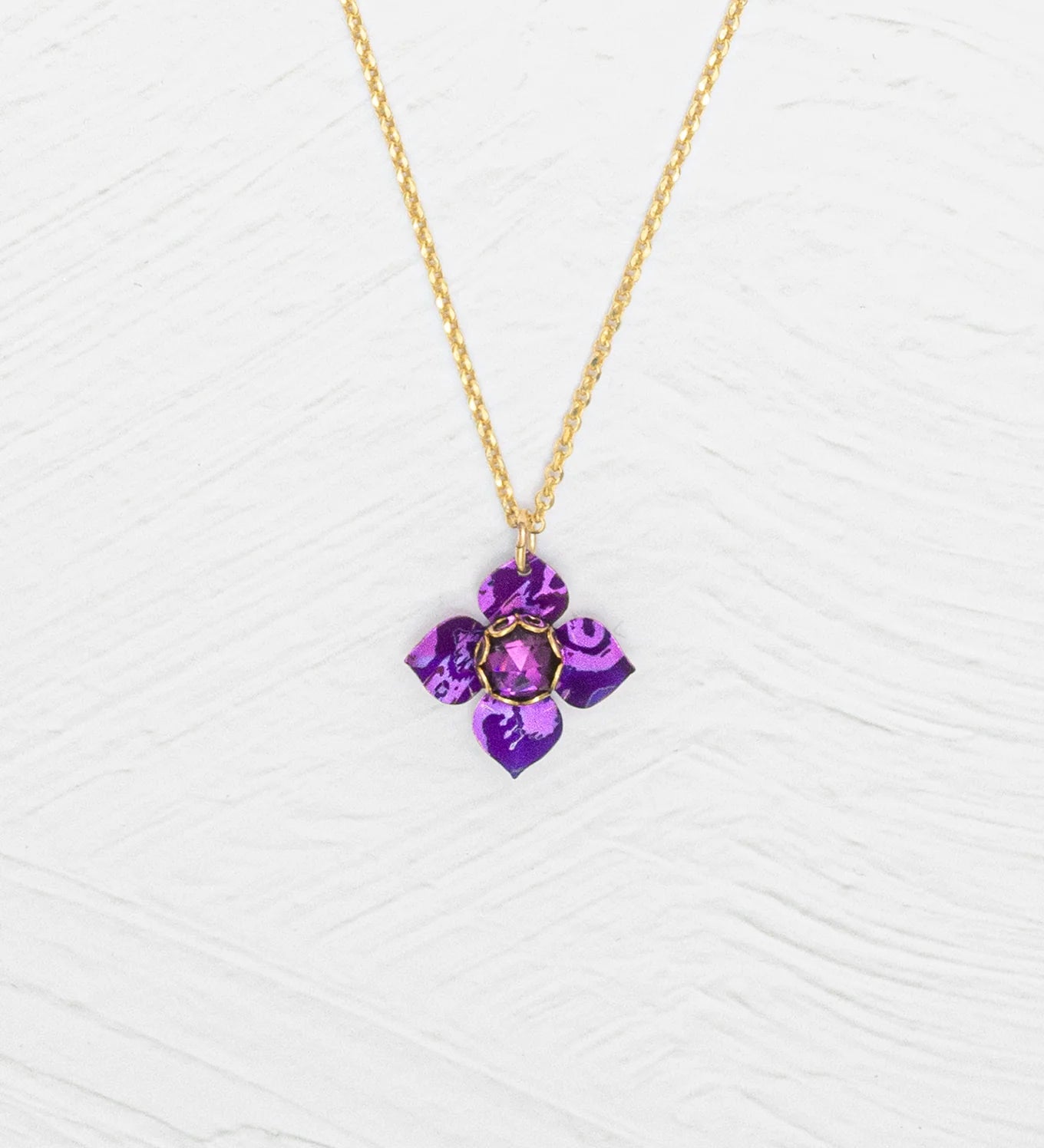 The Petite Fleur Royal Purple Necklace by Holly Yashi features a gold chain and a purple flower-shaped Austrian crystal pendant, shown on a white textured background.