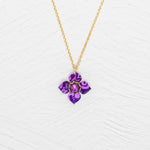 The Petite Fleur Royal Purple Necklace by Holly Yashi features a gold chain and a purple flower-shaped Austrian crystal pendant, shown on a white textured background.