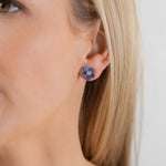 Close-up of a woman wearing Holly Yashi's Petite Plumeria Post Gold/Champagne Earrings—small, flower-shaped studs with gold tones. She has straight blonde hair and light skin against a plain background. Perfect for garden parties.