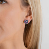 Close-up of a woman wearing Holly Yashi's Petite Plumeria Post Gold/Champagne Earrings—small, flower-shaped studs with gold tones. She has straight blonde hair and light skin against a plain background. Perfect for garden parties.
