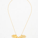 The Holly Yashi Aster Necklace-Gold Necklace features a delicate chain and a sunburst-shaped pendant with textured rays and sparkling crystal stones, beautifully displayed on a light background.