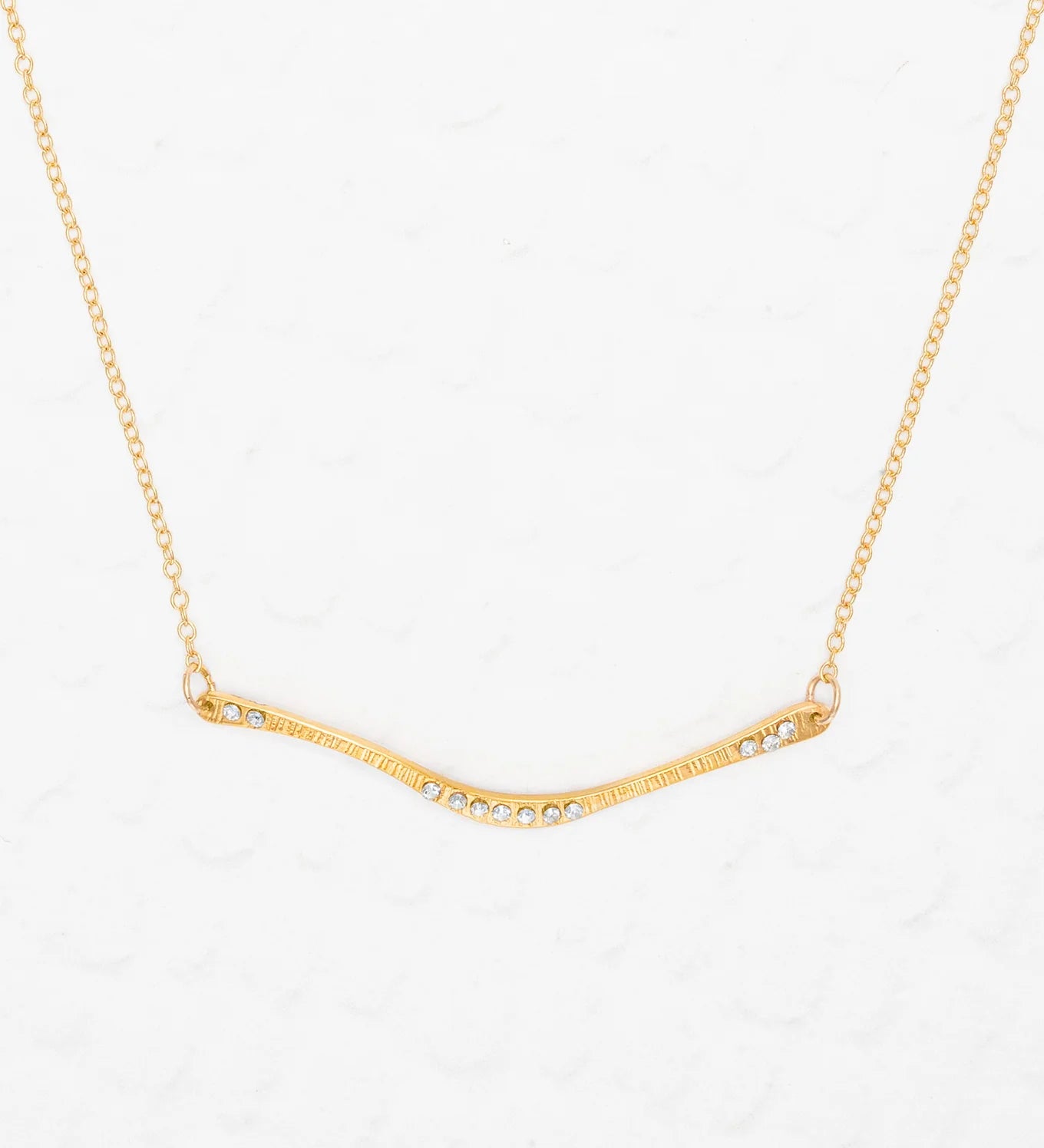 The Holly Yashi Zara Bar Gold Necklace features a slender, curved gold bar with clear gemstones. This hypoallergenic, minimal design is an elegant statement piece for any occasion.