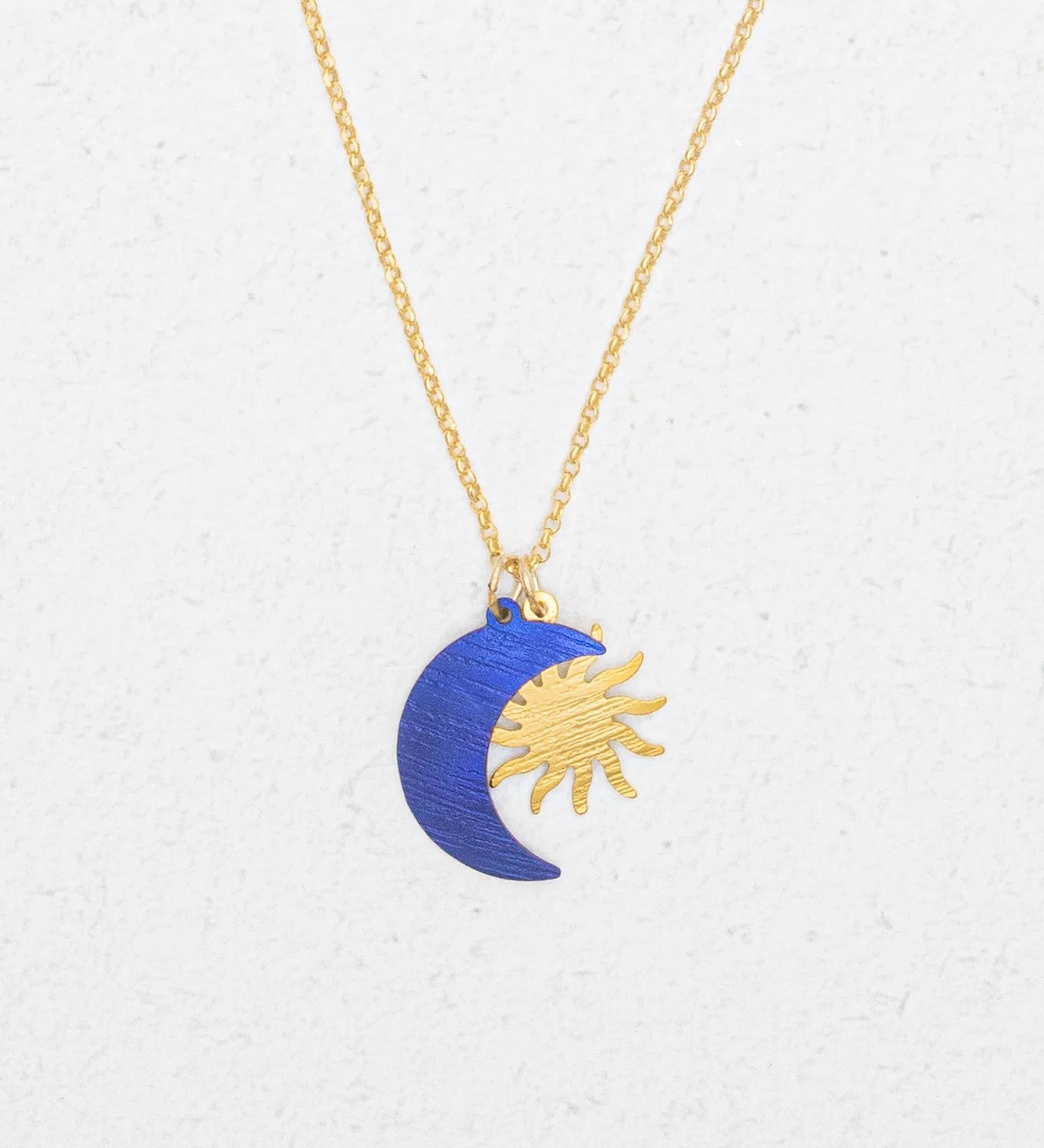 The Holly Yashi Sun and Moon Midnight Blue Necklace features a gold sun and a blue crescent moon pendant, displayed on a white textured background.