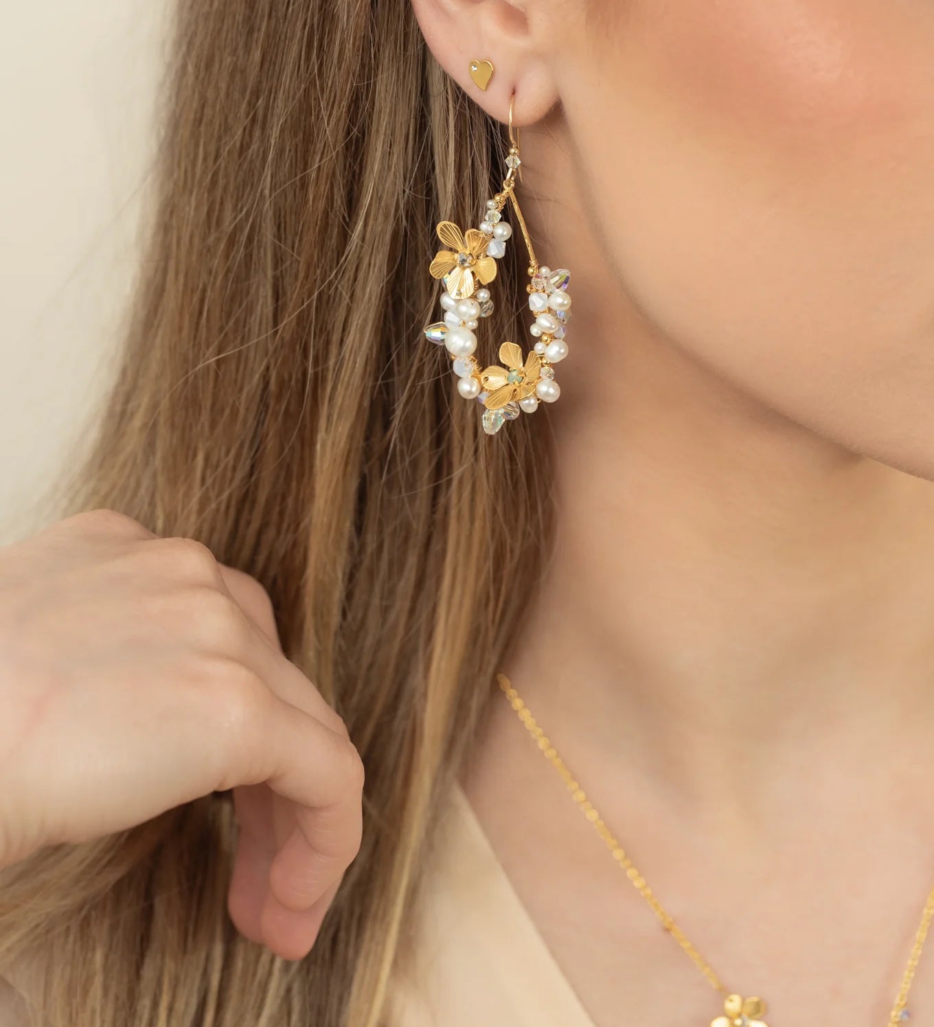 A woman with long, light brown hair wears Holly Yashi's Rafaela Gold & White Earrings. Her hand rests near her cheek, partially obscuring her face, while gold and white accents catch the light.