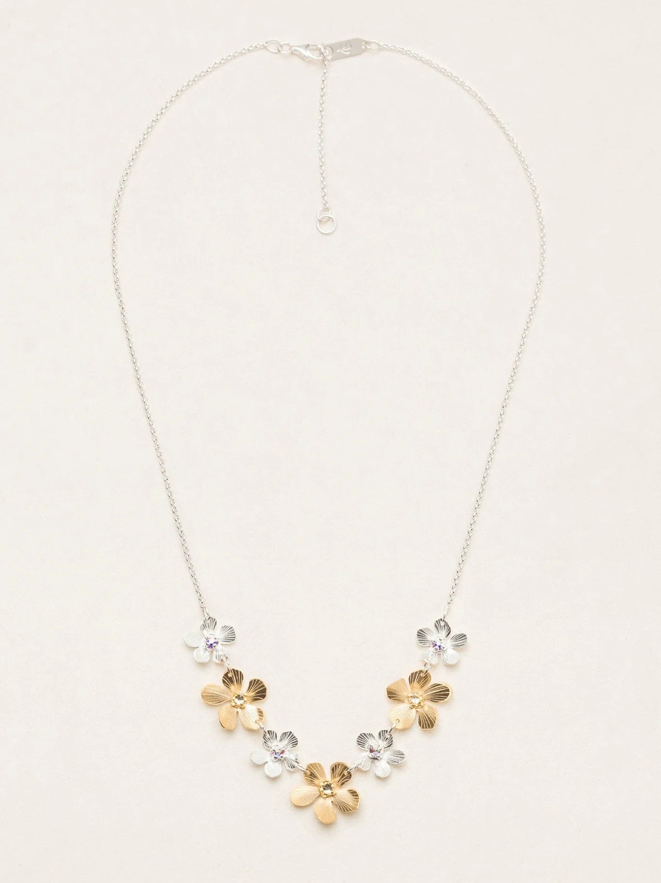 The Plumeria Classic Silver/Gold Necklace by Holly Yashi features a silver chain with five handcrafted floral pendants—three gold, two silver—in a V-shape and an adjustable clasp for the perfect fit.