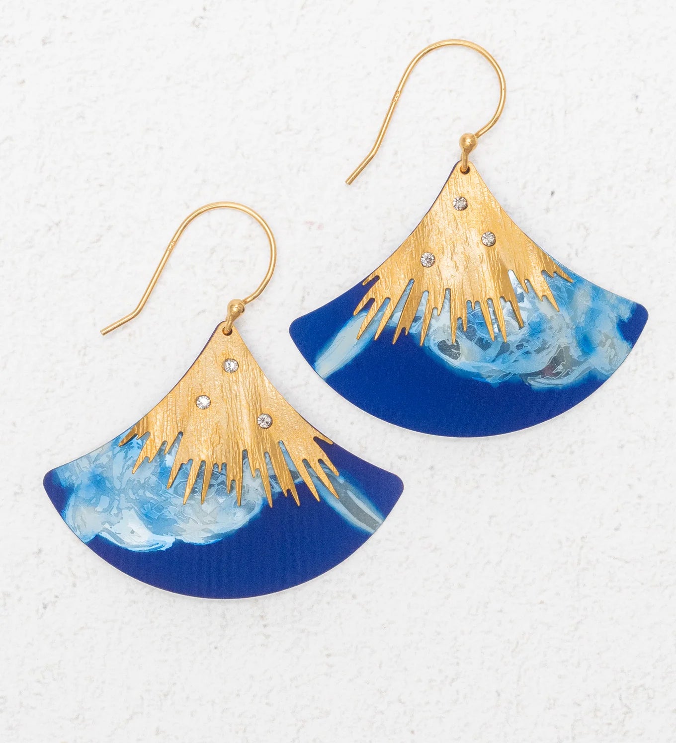 The Aster Earrings/ Midnight Blue by Holly Yashi feature fan-shaped gold hooks, a gold sunburst design, rhinestones, and a marbled midnight blue lower half. Hypoallergenic for comfort. Shown on a white textured background.