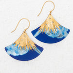 The Aster Earrings/ Midnight Blue by Holly Yashi feature fan-shaped gold hooks, a gold sunburst design, rhinestones, and a marbled midnight blue lower half. Hypoallergenic for comfort. Shown on a white textured background.
